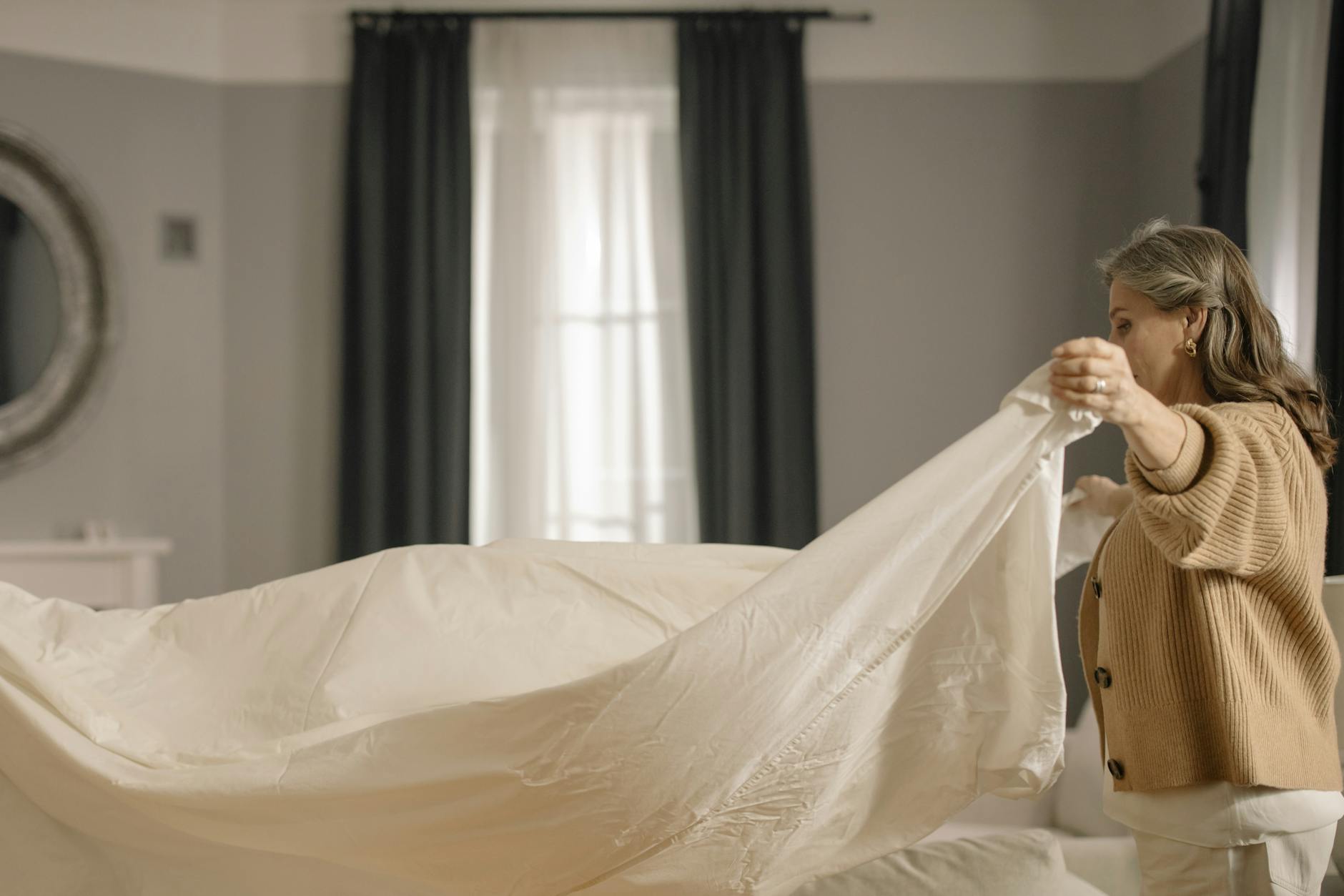 Jak często zmieniać prześcieradło i dlaczego ma to ogromne znaczenie dla zdrowia Starsza kobieta starannie ścieli łóżko w jasnej, uporządkowanej sypialni